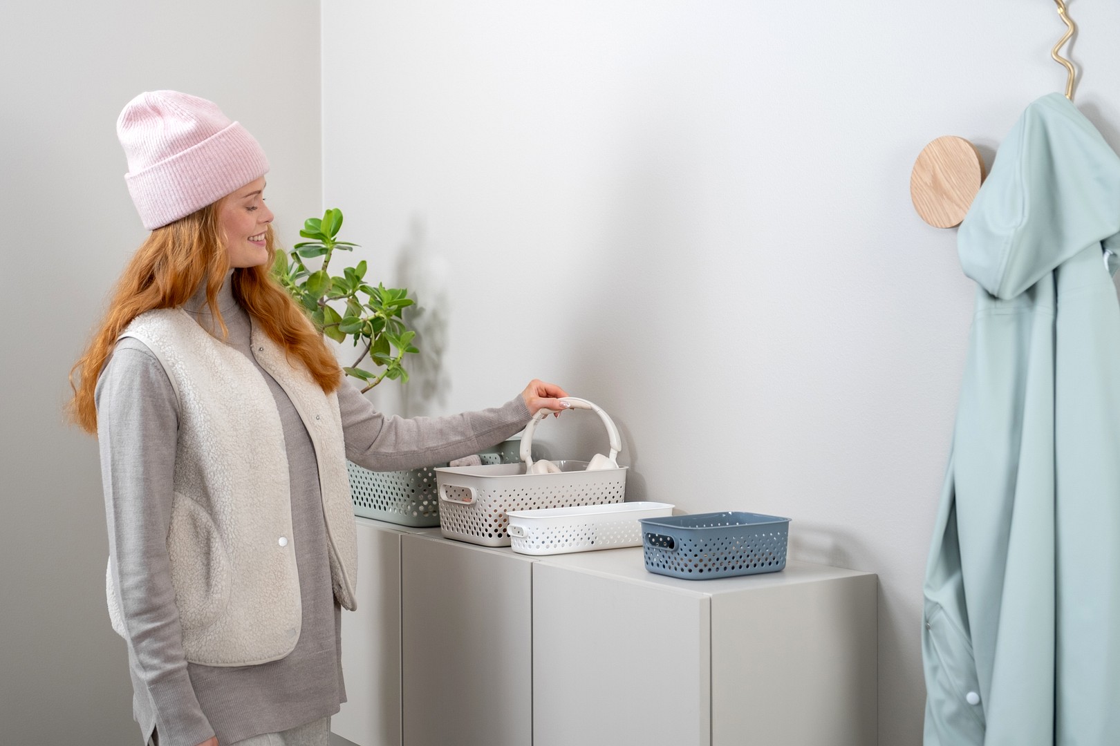 A woman placing headphones to SmartStore Essence storage basket on a hallway countertop